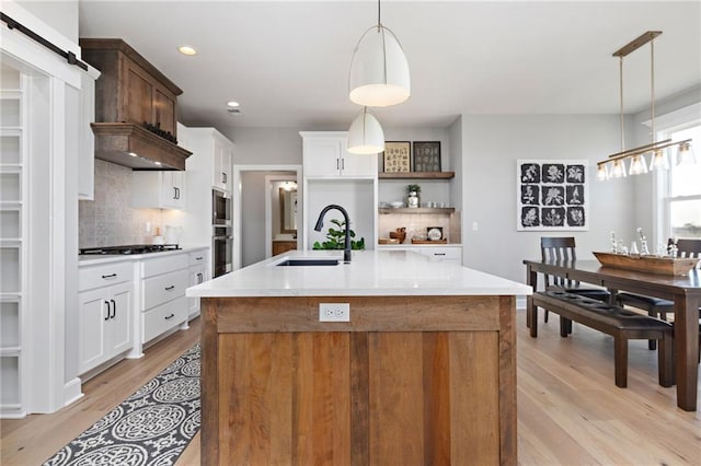 kitchen with white cabinetry, sink, decorative light fixtures, and a center island with sink