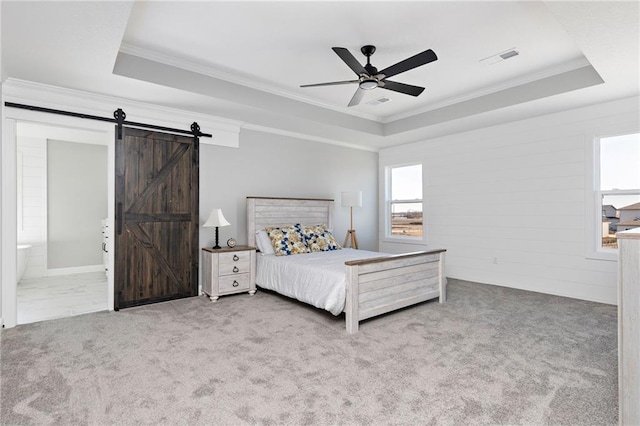 carpeted bedroom featuring ornamental molding, a barn door, ceiling fan, and a tray ceiling