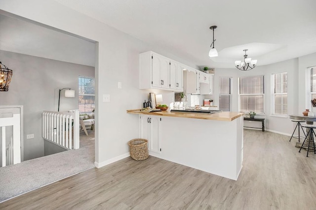 kitchen featuring white cabinetry, kitchen peninsula, butcher block countertops, a chandelier, and pendant lighting