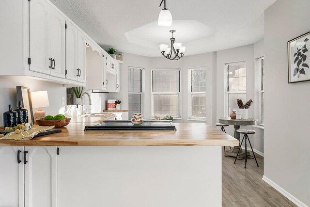 kitchen featuring wooden counters, a raised ceiling, sink, hanging light fixtures, and white cabinets