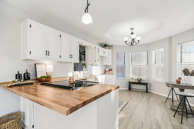 kitchen featuring wooden counters, kitchen peninsula, a tray ceiling, hanging light fixtures, and white cabinets