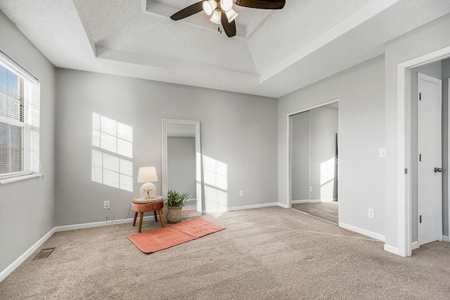 interior space featuring light carpet, ceiling fan, a tray ceiling, and a textured ceiling