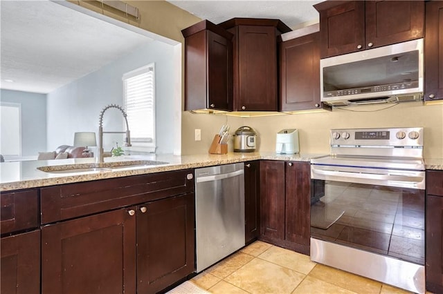 kitchen featuring appliances with stainless steel finishes, sink, light tile patterned floors, and light stone counters