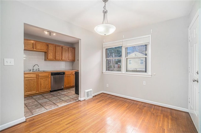 kitchen with backsplash, light wood-type flooring, pendant lighting, stainless steel dishwasher, and sink