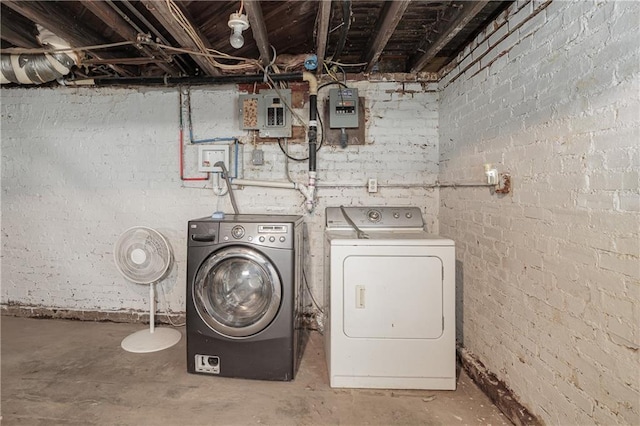 clothes washing area featuring brick wall, washer and dryer, and electric panel