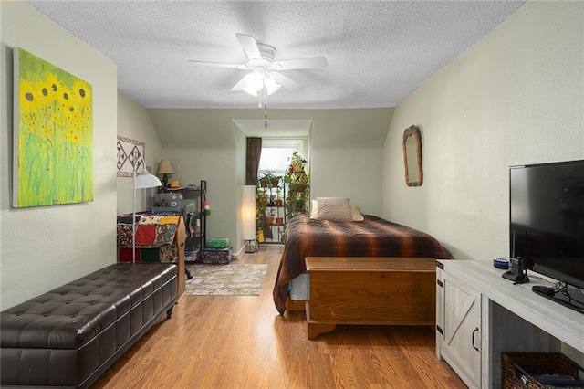 bedroom featuring ceiling fan, light wood-type flooring, a textured ceiling, and lofted ceiling