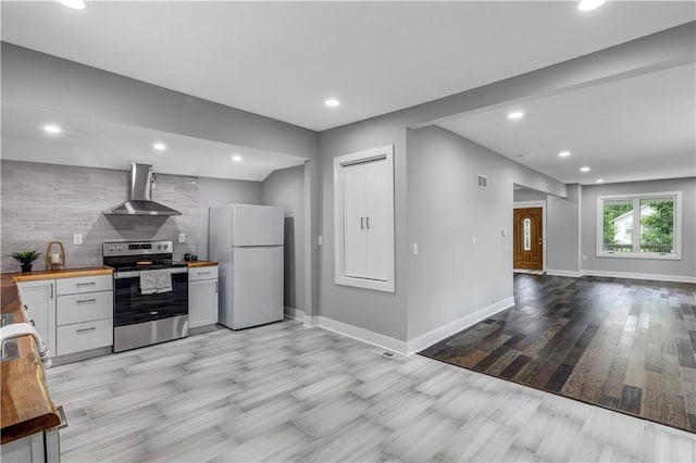 kitchen with stainless steel electric stove, wall chimney exhaust hood, white cabinets, butcher block countertops, and white fridge