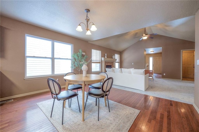 dining room with light hardwood / wood-style floors, a textured ceiling, lofted ceiling, and ceiling fan with notable chandelier