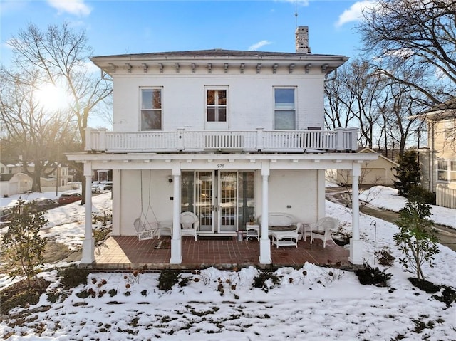 snow covered rear of property featuring french doors and a balcony