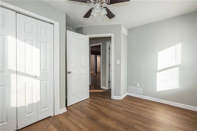 unfurnished bedroom featuring ceiling fan, multiple windows, dark hardwood / wood-style flooring, and a closet