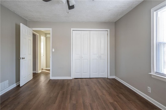 unfurnished bedroom with ceiling fan, a closet, dark wood-type flooring, and multiple windows