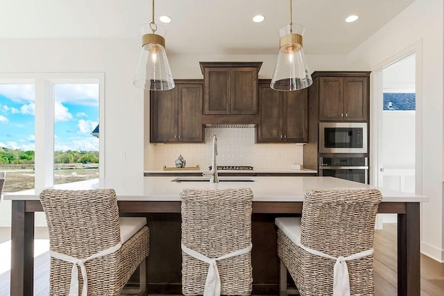 kitchen with pendant lighting, sink, dark brown cabinetry, stainless steel oven, and built in microwave