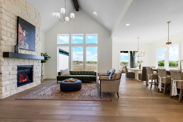 living room featuring beam ceiling, plenty of natural light, a stone fireplace, and a chandelier