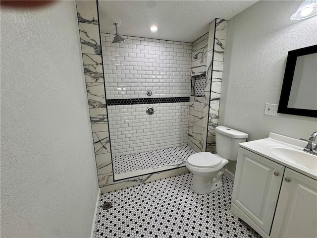 bathroom featuring a textured ceiling, toilet, vanity, and a tile shower