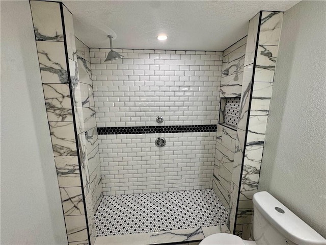 bathroom with toilet, tiled shower, and a textured ceiling