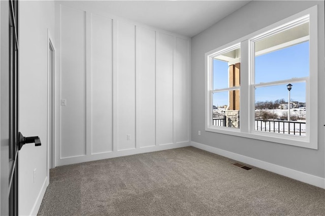 spare room with a decorative wall, carpet flooring, visible vents, and baseboards