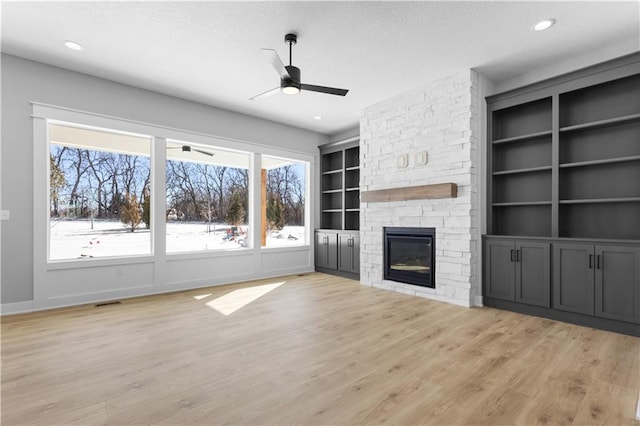 unfurnished living room featuring light wood-style floors, recessed lighting, a ceiling fan, and a stone fireplace