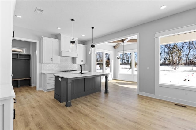 kitchen featuring white cabinetry, light countertops, an island with sink, a kitchen bar, and decorative light fixtures