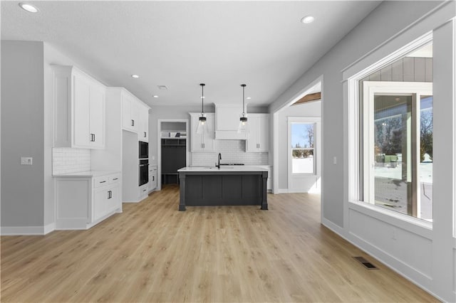 kitchen with an island with sink, pendant lighting, light countertops, and white cabinets