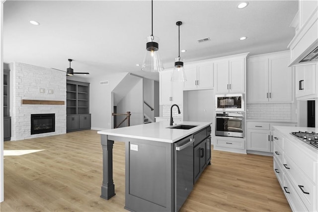 kitchen with white cabinets, light countertops, a center island with sink, and a sink