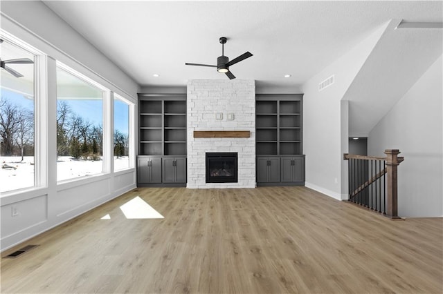 unfurnished living room featuring light wood-style flooring, a fireplace, visible vents, and a ceiling fan