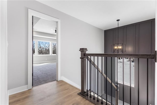 corridor featuring baseboards, light wood-style flooring, an upstairs landing, and an inviting chandelier