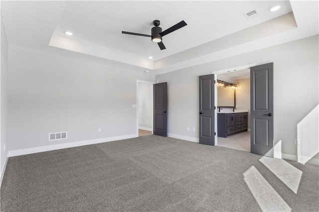 unfurnished bedroom featuring baseboards, visible vents, a raised ceiling, and light colored carpet