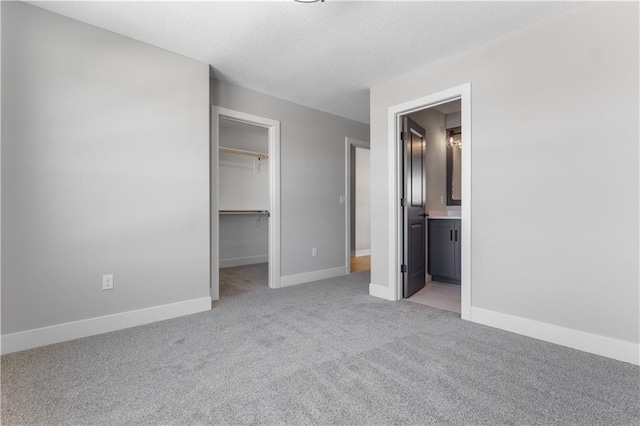 unfurnished bedroom featuring a closet, light colored carpet, a spacious closet, a textured ceiling, and baseboards