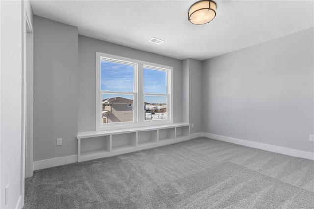 spare room featuring carpet, visible vents, a textured ceiling, and baseboards