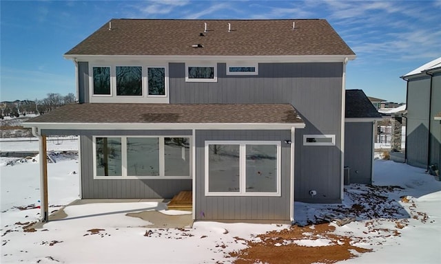 snow covered rear of property with a shingled roof