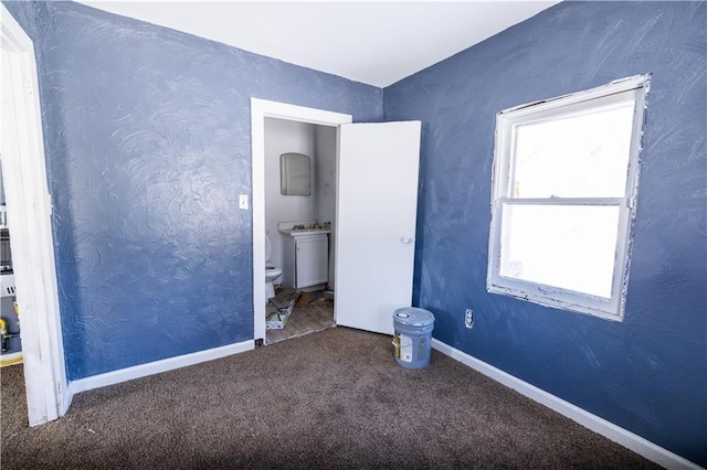 unfurnished bedroom with connected bathroom and dark colored carpet