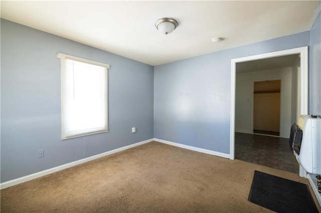 empty room with baseboards, carpet flooring, and heating unit