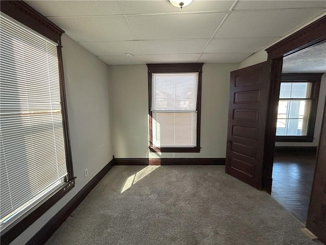 empty room with a drop ceiling, a wealth of natural light, and dark colored carpet