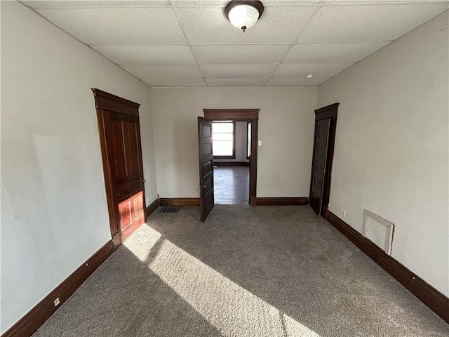 unfurnished room with dark colored carpet and a drop ceiling