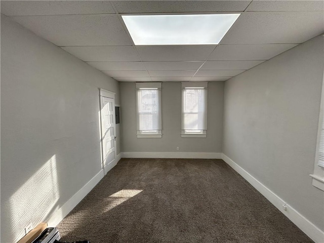 spare room featuring a paneled ceiling and dark carpet