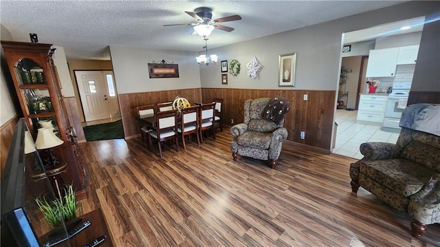 living room featuring ceiling fan with notable chandelier, a textured ceiling, and light hardwood / wood-style floors