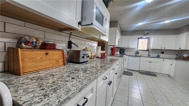 kitchen featuring white cabinetry, backsplash, white appliances, light tile patterned flooring, and light stone counters