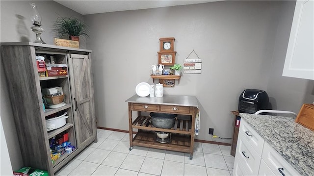 interior space featuring white cabinets, light tile patterned flooring, and light stone counters