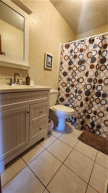 bathroom with a textured ceiling, toilet, vanity, and tile patterned flooring