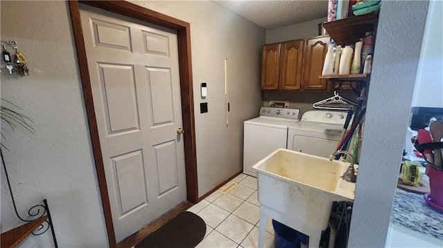 laundry area featuring a textured ceiling, cabinets, sink, independent washer and dryer, and light tile patterned flooring