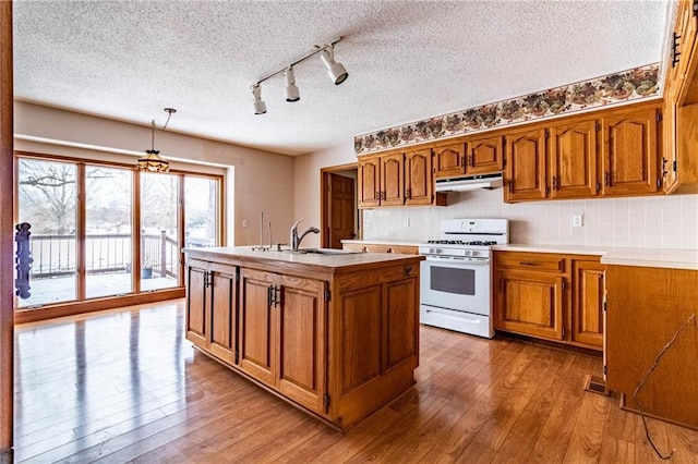 kitchen with decorative light fixtures, tasteful backsplash, a center island with sink, sink, and white range with gas cooktop