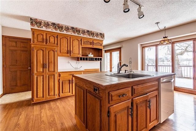 kitchen featuring tile countertops, stainless steel dishwasher, sink, an island with sink, and a textured ceiling