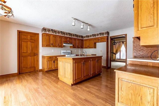 kitchen featuring light wood-type flooring, white stove, an island with sink, and a textured ceiling