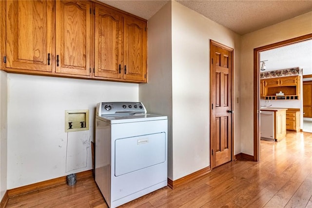 washroom featuring a textured ceiling, cabinets, light hardwood / wood-style flooring, and washer / clothes dryer