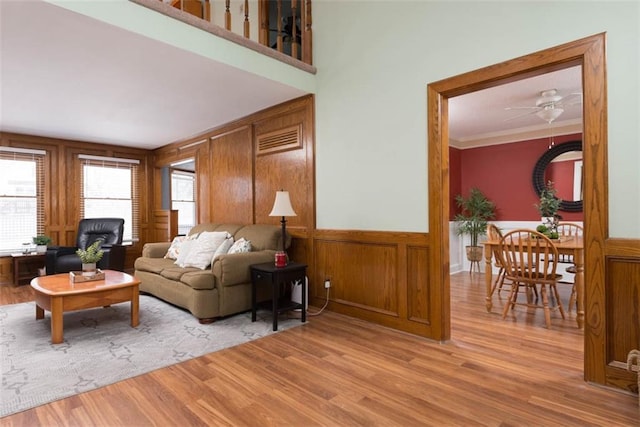 living room featuring ceiling fan, crown molding, light hardwood / wood-style flooring, and wooden walls