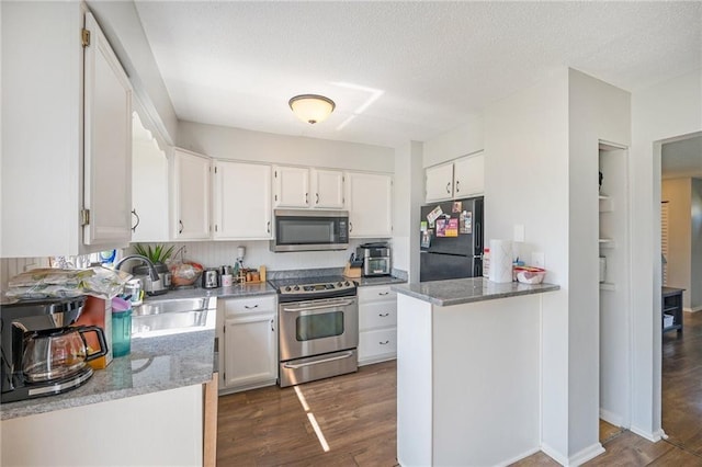 kitchen with white cabinets, dark hardwood / wood-style flooring, stainless steel appliances, dark stone counters, and sink