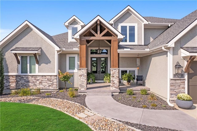 entrance to property with stone siding, french doors, a shingled roof, and stucco siding