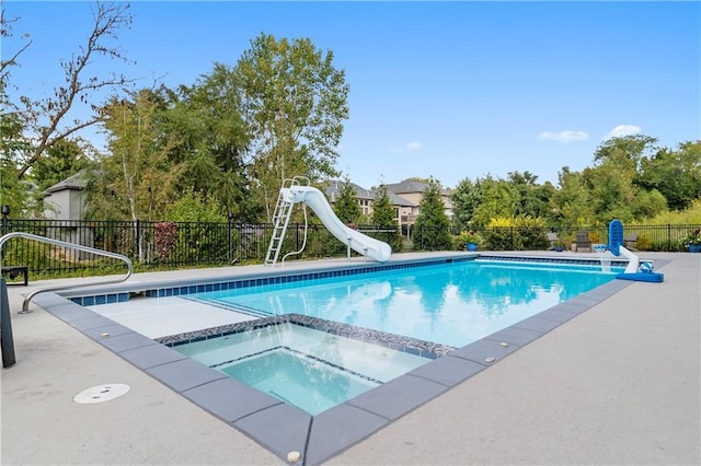 view of swimming pool with a patio, fence, a water slide, a pool with connected hot tub, and a sink