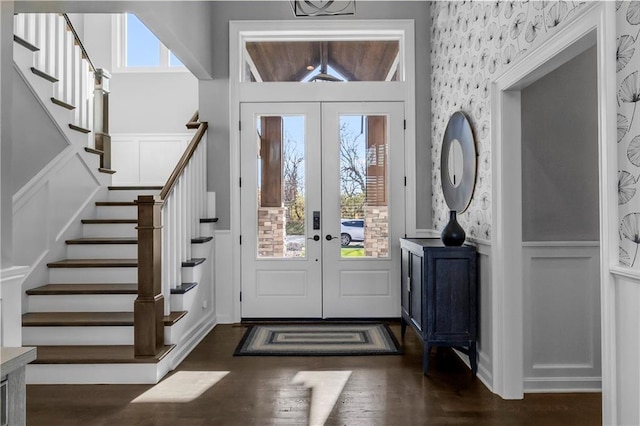 foyer featuring a wainscoted wall, french doors, dark wood-type flooring, and stairway