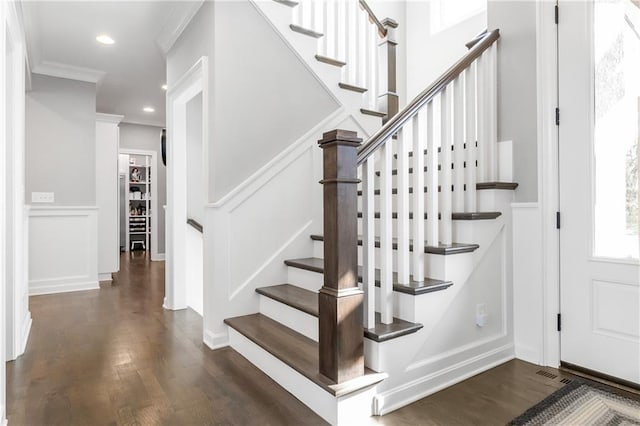 stairs with recessed lighting, a wainscoted wall, a decorative wall, wood finished floors, and ornamental molding